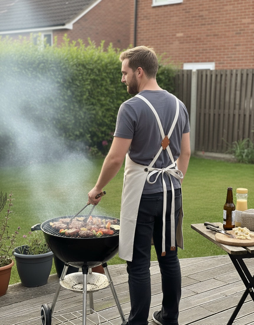 Waterproof cotton canvas apron in tan brown with adjustable neck strap and spacious front pockets, styled flat on rustic wooden background.