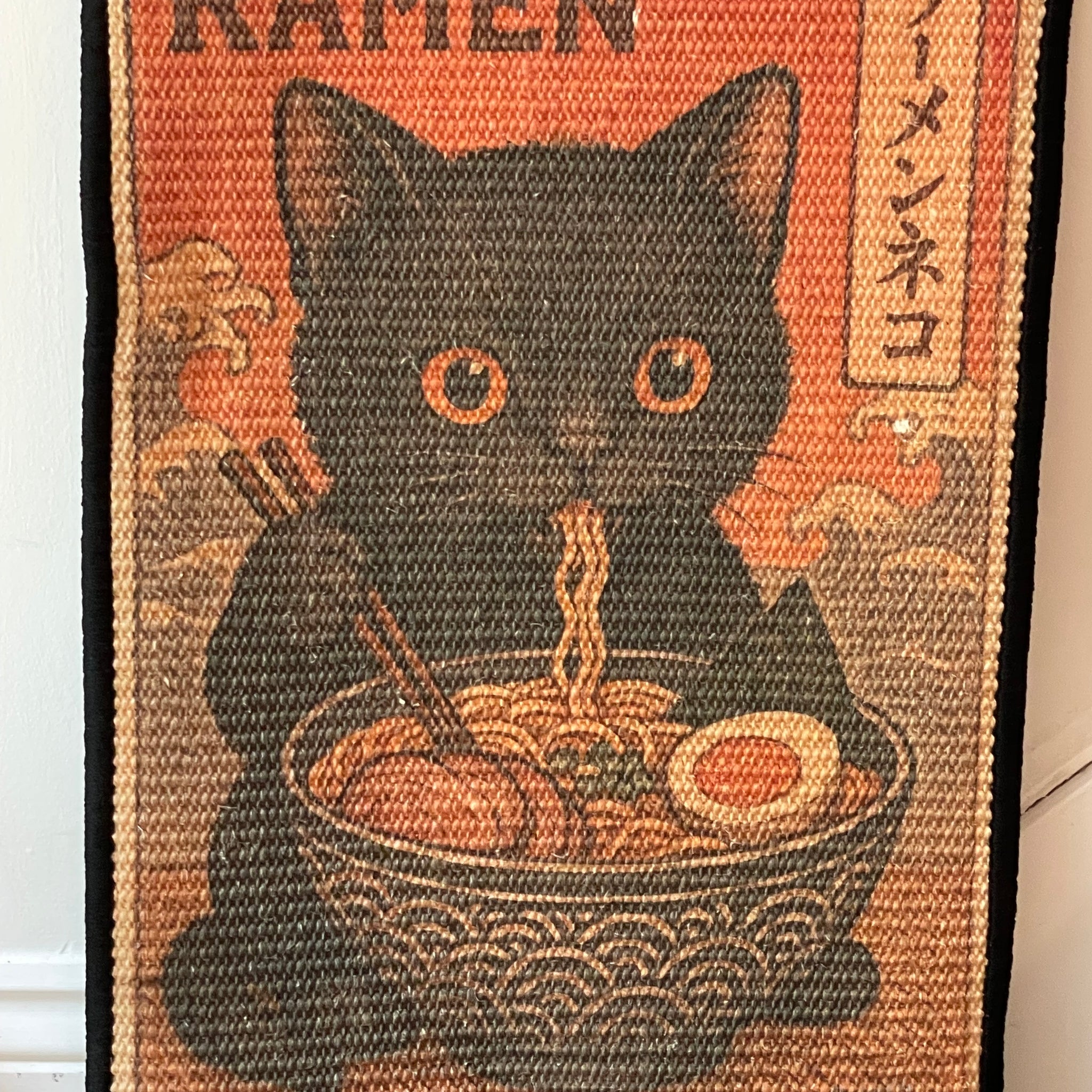 Doormat with a black cat design and ramen bowl on a red background