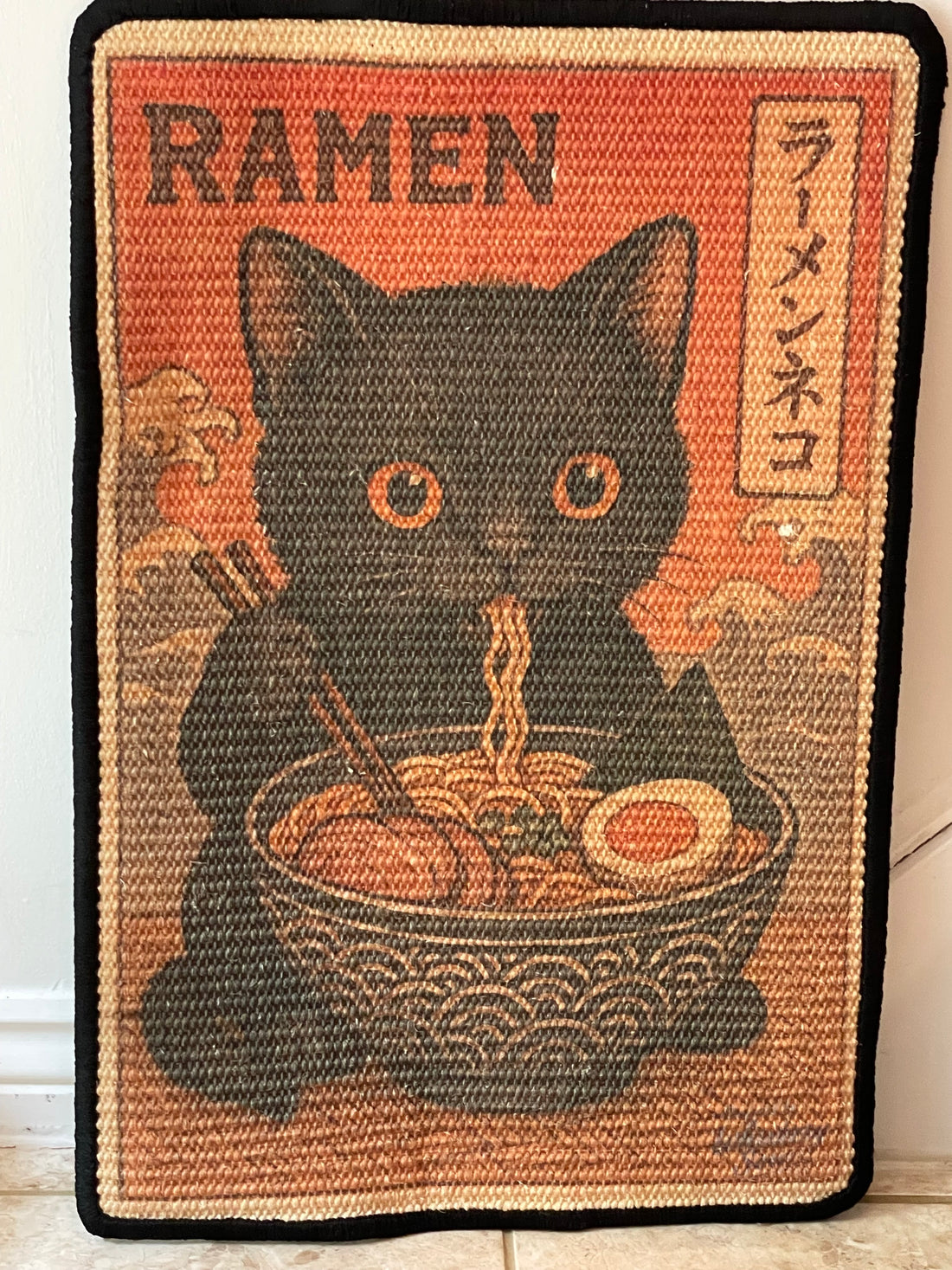 Doormat with a black cat design and ramen bowl on a red background