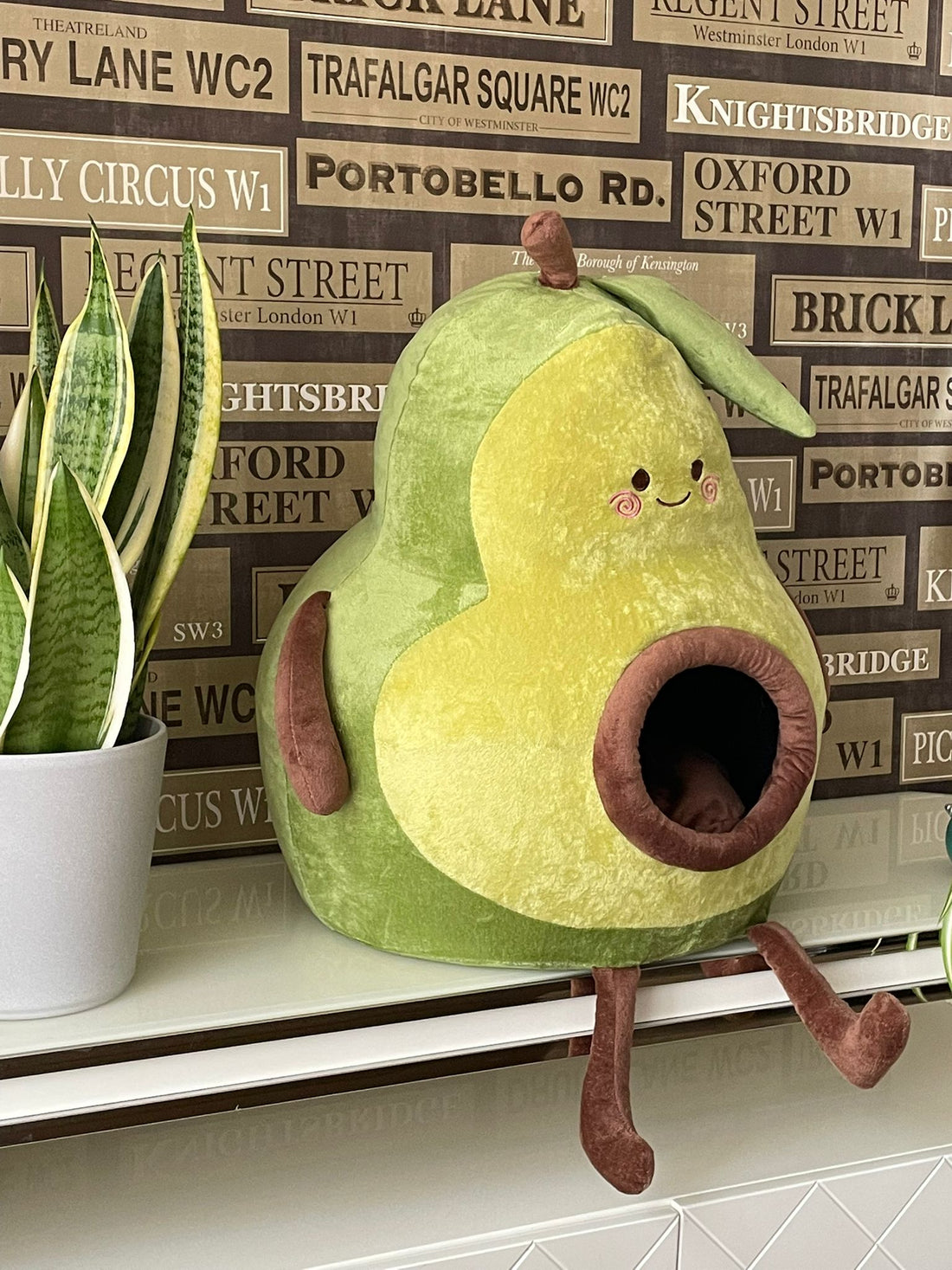 Cosy avocado-shaped plush cat house with a cat peeking out, on a wooden sideboard