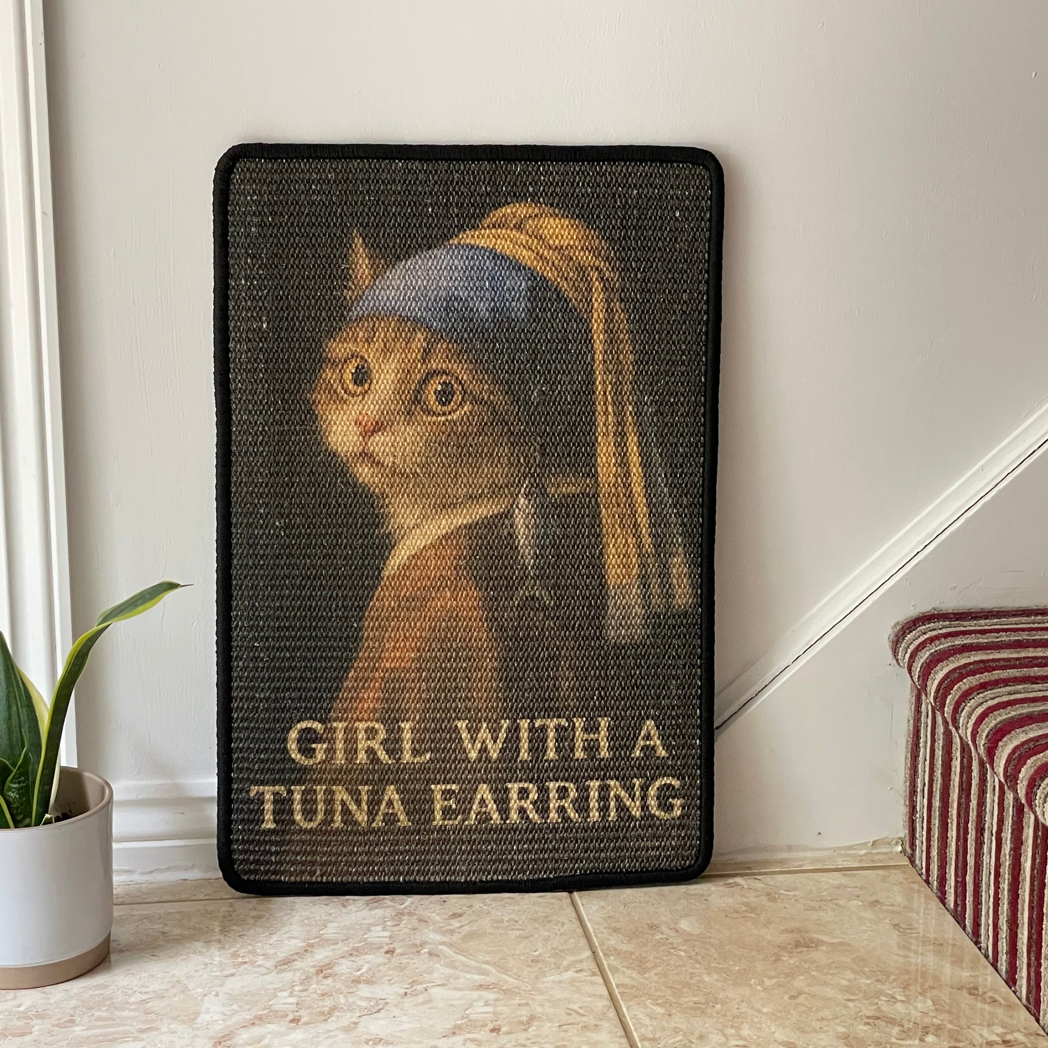 Decorative wall art with a cat wearing a tuna earring, titled 'Girl with a Tuna Earring', on a plain wall.
