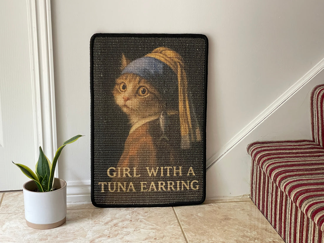 Decorative wall art with a cat wearing a tuna earring, titled 'Girl with a Tuna Earring', on a plain wall.