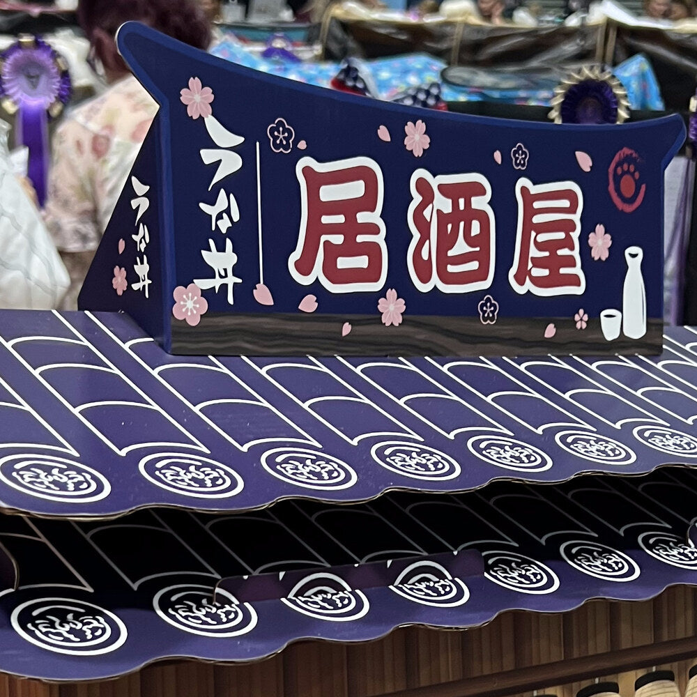 The Neko-ya signboard with red 居酒屋 kanji on an indigo banner with sakura blossoms