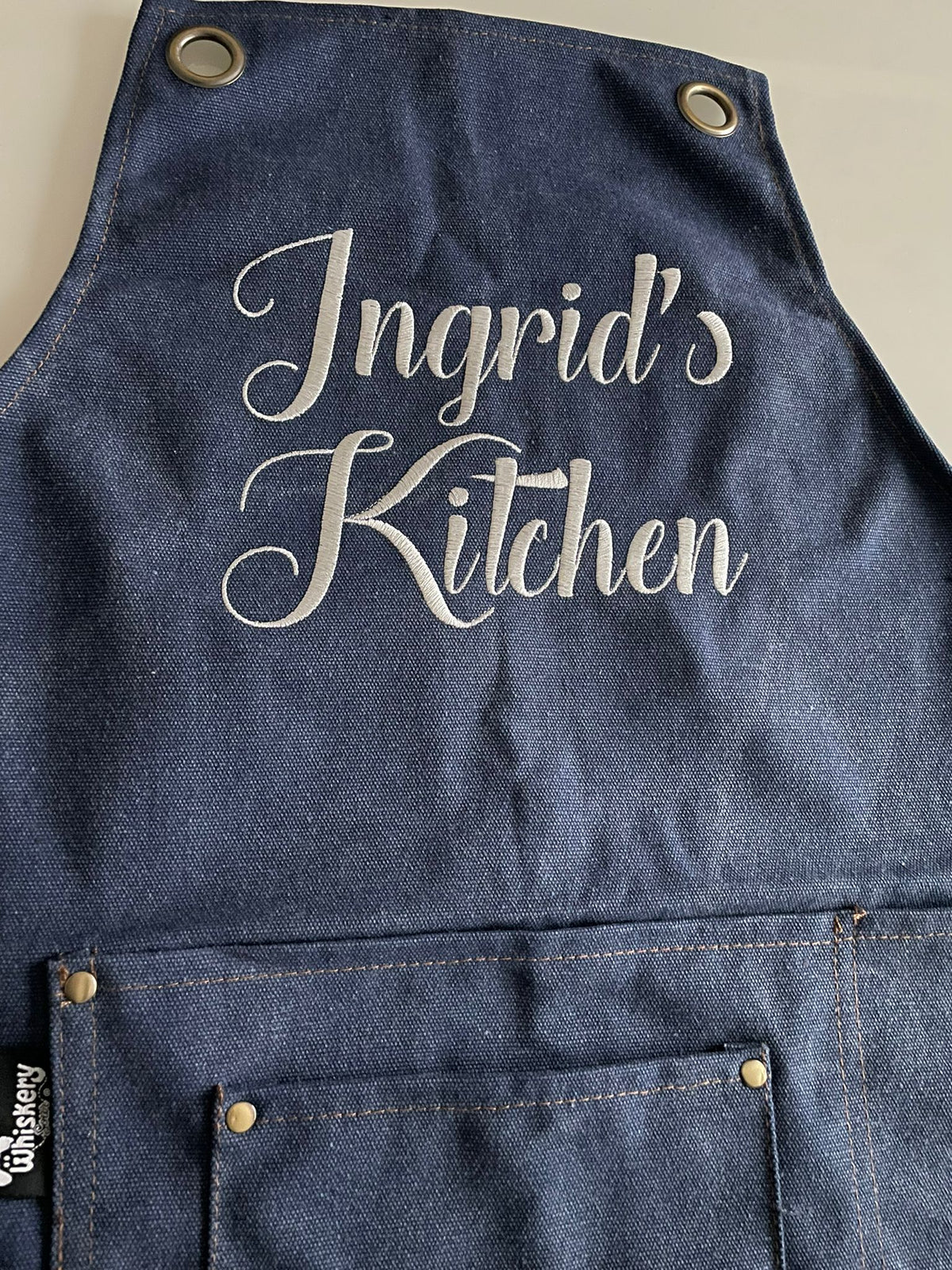 Navy canvas apron embroidered with Ingrid's Kitchen in white script — personalised cooking apron | Whiskery Sour