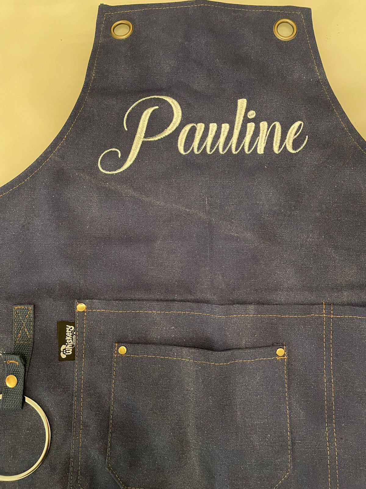 Grey canvas apron with the name Pauline embroidered in cream script across the bib | Whiskery Sour